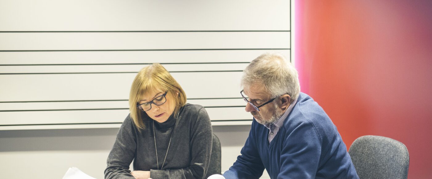 Man and woman sitting at desk pointing at table of work sheets on desk