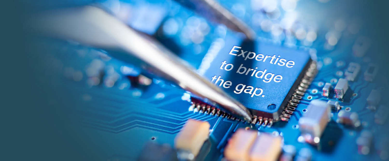 An embossed mircochip which says Expertise to bridge the Gap being placed on a circuit board with an with a pair of tweezers
