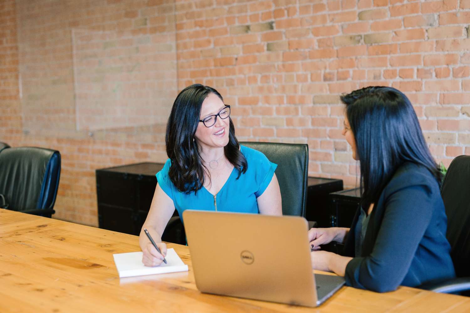 Woman in teal t shirt sitting beside woman in black suit